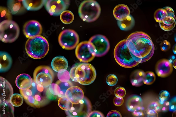 Fototapeta Floating colorful bubbles isolated on black background with iridescent reflections. Blowing soap bubbles is a popular kids enjoyment for parties or fun fairs and a symbol of grace and fragility. 