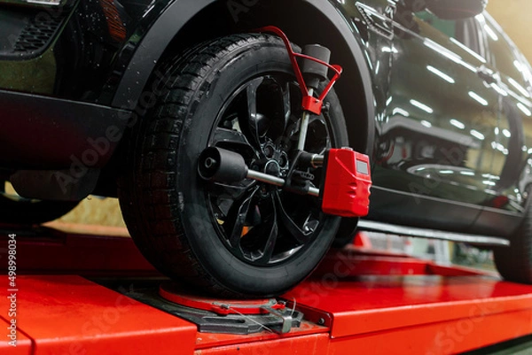 Fototapeta Car mechanic installing wheel alignment sensors, car suspension adjustment. Car mechanic at work