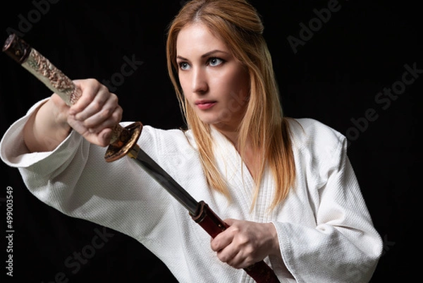 Fototapeta A young girl holds a Japanese katana sword in her hands
