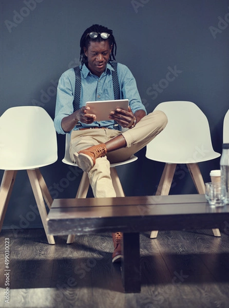 Obraz Using this time to catch up on social media. Shot of a young businessman using a tablet while waiting for an interview.