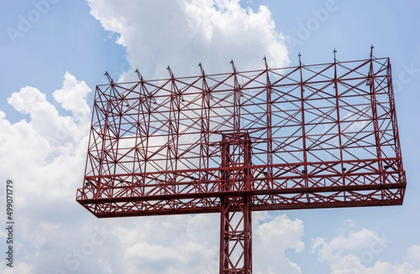 Fototapeta A view of an old sign, a red steel structure towering in anticipation of an advertisement.