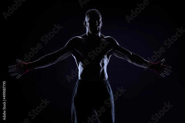 Fototapeta Kickboxer in red bandages poses on a blue background with his arms apart. The concept of mixed martial arts