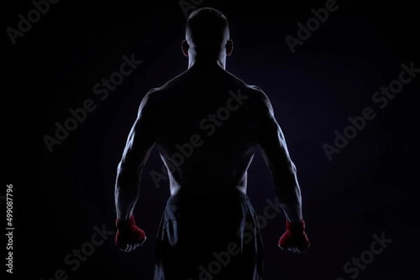 Obraz Kickboxer in red bandages posing on a blue background. Back view. The concept of mixed martial arts.