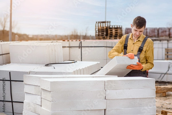 Fototapeta  man contractor builder is holding an autoclaved aerated concrete block aac on a construction site.