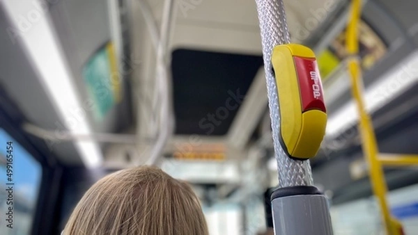 Fototapeta Red and yellow "Stop" request button on a public bus with shallow focus and partial view of a traveler's hair