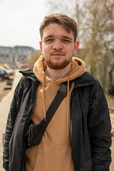 Fototapeta guy with a beard looks dreamily into the camera in a jacket pimples on the face portrait
