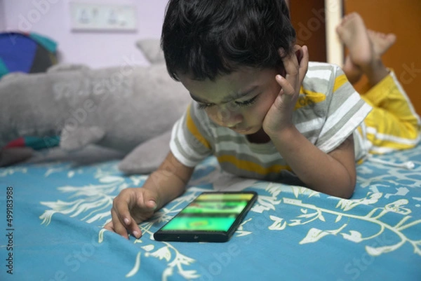 Obraz a toddler baby boy engaged in watching and exploring mobile phone.Screen time addiction concept image