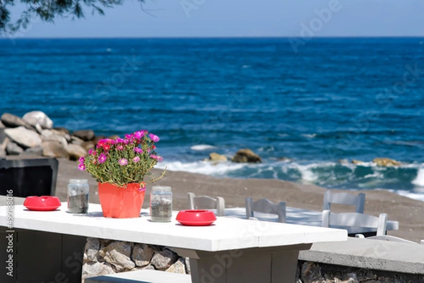 Fototapeta A beautiful outdoor bar decorated with flowers and ashtrays with an amazing view of the famous beach of Perissa in Santorini