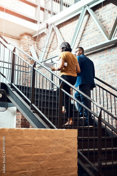Fototapeta Taking the stairway to success. Shot of two designers having a discussion on a staircase in an office.