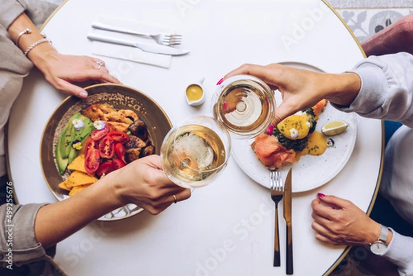 Obraz Friends holding a glass of wine and toasting. Top view of brunch table.