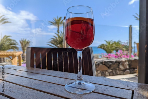Fototapeta Enjoying a glass of sangria in the shade of a restaurant overlooking the sea, flowers and palm trees while on vacation