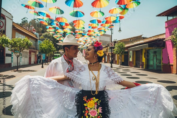 Fototapeta Dancers of typical Mexican dances from the region of Veracruz, Mexico, doing their performance in the street adorned with colored umbrellas.