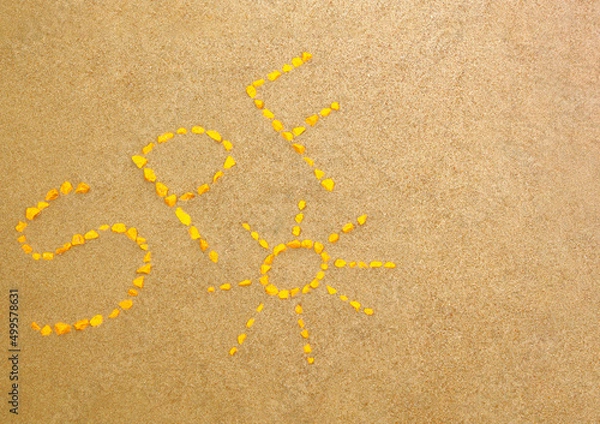Fototapeta SPF letters written by yellow stones on the sand. Sun protect factor skin care concept background with copy space