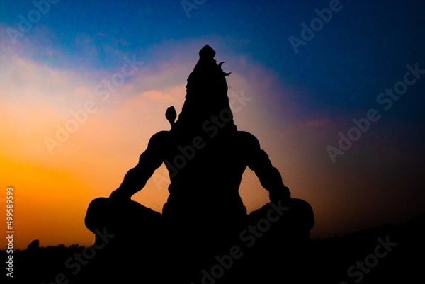 Fototapeta back lit statue of hindu god lord shiva in meditation posture with dramatic sky from unique angle
