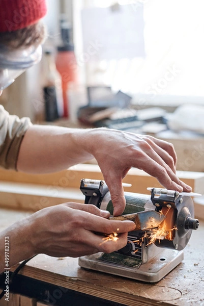 Fototapeta Close-up of unrecognizable man working in woodworking workshop sharpening knife using grinding jig