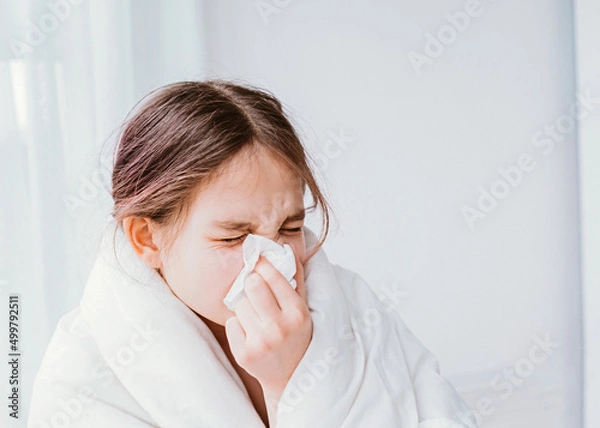 Fototapeta A cold girl blows her nose in a white rag on white background. Rhinitis snot runny nose stuffy nose. Allergy Preteen girl with handkerchief. medical concept