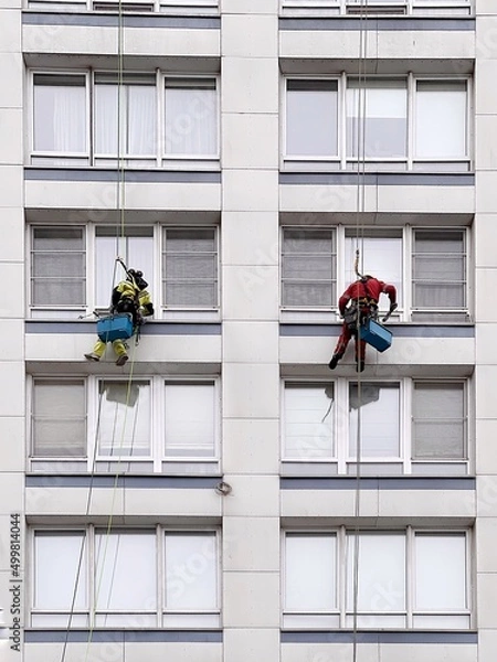 Fototapeta Industrial climbers wash windows on huge residential building. Working at height requires skills and abilities.