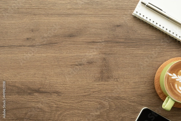 Fototapeta Wood desk table with cup of latte coffee and notebook with pen. Top view with copy space, flat lay.