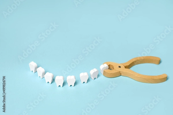 Obraz Tooth extraction with a dental instrument with forceps.  A model of teeth in the shape of a smile. Problems with wisdom teeth, toothache