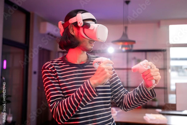 Fototapeta relax casual Asian adult Man Wearing Virtual Reality Headset and Holding Controllers Plays in a boxing sport Video Game at Home. Playing VR active sport game online in the Living Room with rgb lightin