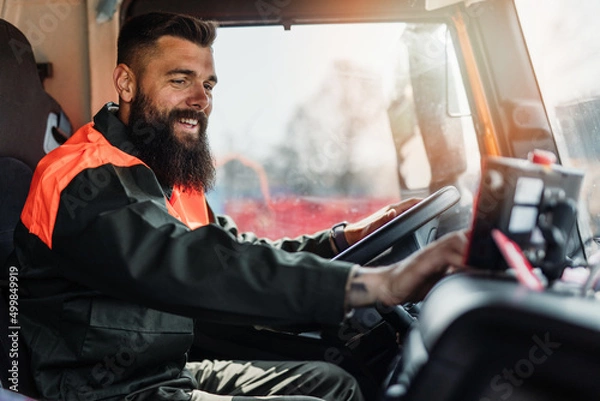 Fototapeta Young garbage removal worker driving a waste truck