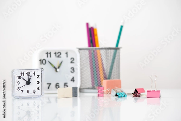 Fototapeta on the table there are two clocks of different sizes, a glass with colored pencils. there are a lot of colored stationery pins, two grinders and a gray pencil sharpener.