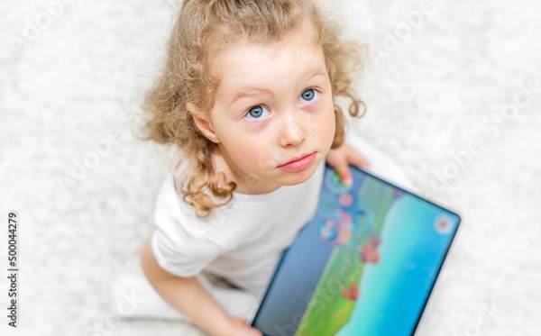 Fototapeta The child enthusiastically plays on the tablet.