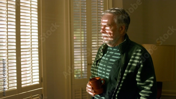 Obraz senior man drinking coffee next to a window