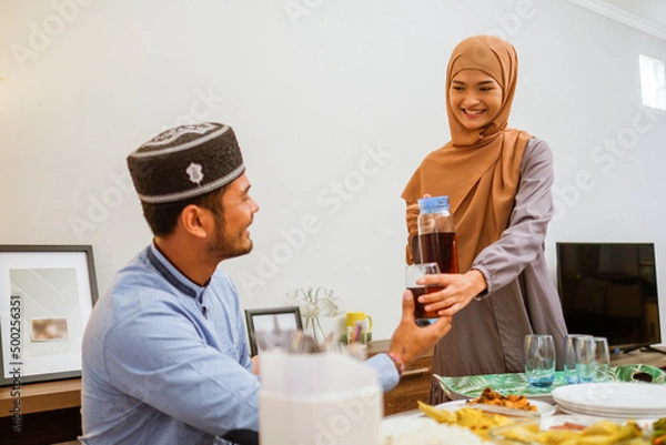 Fototapeta excited asian muslim woman served the food for friend while sitting on dining table for iftar or eid mubarak gathering at home