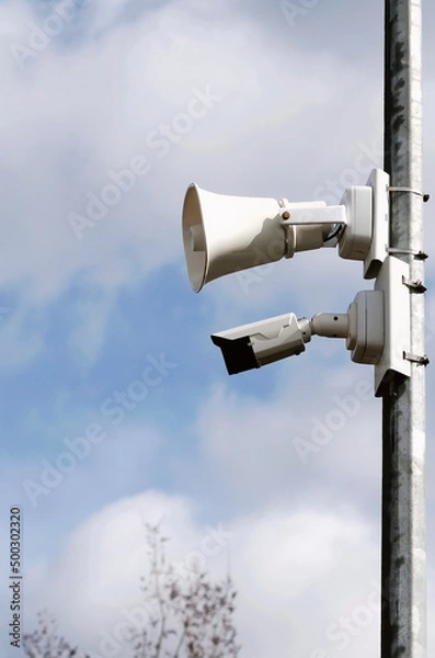 Fototapeta Loudspeaker and video camera on a wooden pole against the blue sky. Vertical photography.
