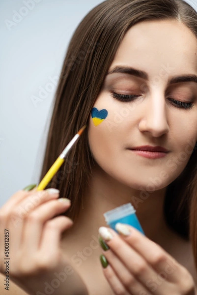 Obraz A young girl with beautiful skin draws a heart from the colors of the Ukrainian flag, no war