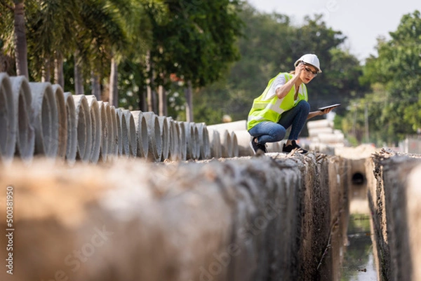 Fototapeta Woman construction site engineer architect worker with hard hat using tablet for checking concret pipes