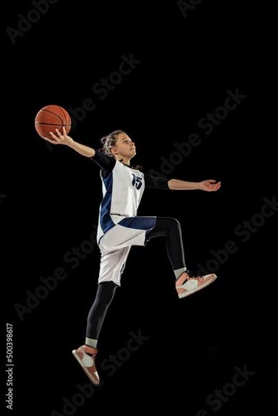 Fototapeta Jump shot. Scoring a goal. Portrait of teen girl, basketball player in motion, training, playing isolated over black background.