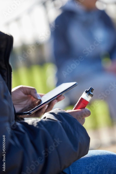 Obraz Close Up Of Teenagers With Mobile Phone Vaping  In Park