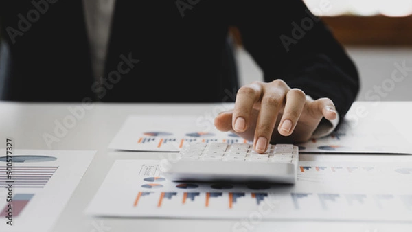 Fototapeta Businessman using a calculator to calculate numbers on a company's financial documents, he is analyzing historical financial data to plan how to grow the company. Financial concept.