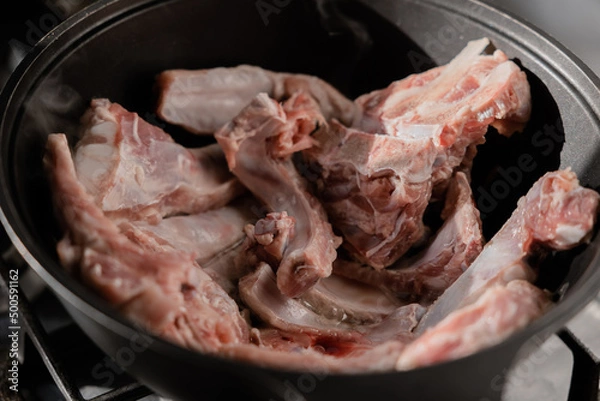 Fototapeta Chopped onions and pieces of meat are fried in boiling oil. Cooking pilaf in a cauldron, a step-by-step recipe for real pilaf.