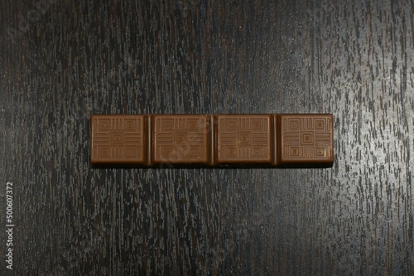 Fototapeta a small bar of milk chocolate on a brown table