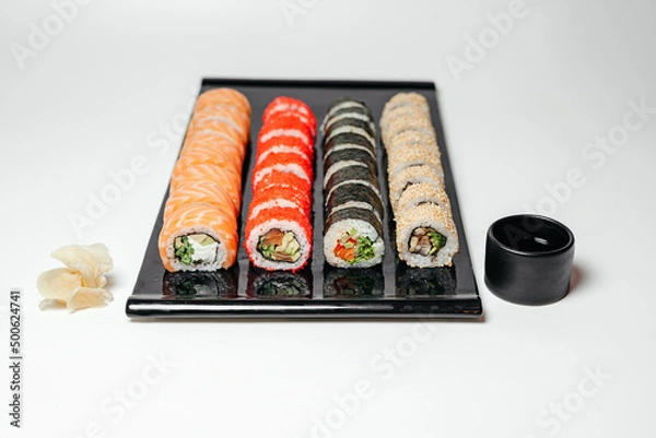 Fototapeta Sushi, rolls. Chinese and Asian cuisine, sets of rolls of ginger and soy sauce lie on a black board with chopsticks. Sushi is made in sets