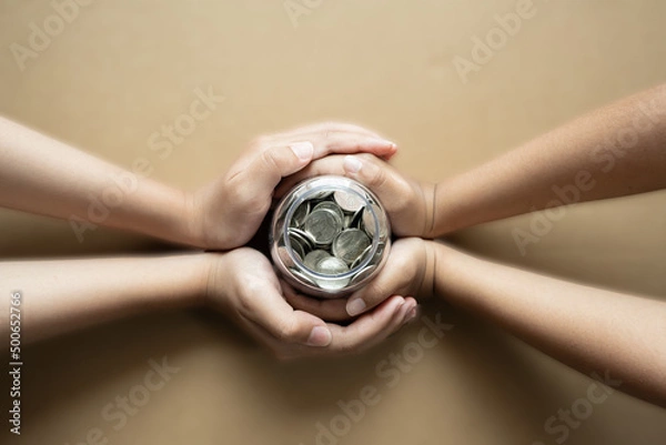 Fototapeta Kid hands holding coins in a jar together as saving concept for family or education.