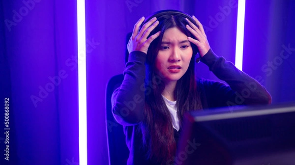 Fototapeta Stressed Boring and loses. Young pretty asian woman playing game computer pc. Female Gamer on headphone playing video game  feeling sadness. Loss and Missed the chance to become a champion