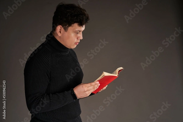 Obraz Latin man reading a red book, isolated on gray background