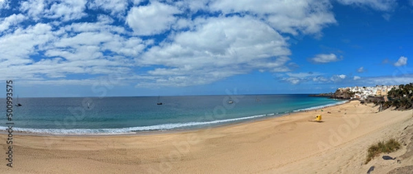 Fototapeta Beautiful panoramic view of long wide morro jable beach on fuerteventura island under a blue cloudy sky with less people and some boats