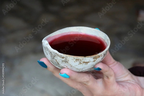 Fototapeta A woman's hand holds a bowl with a red Mayan ritual drink. Ancient shell with hibiscus tea.