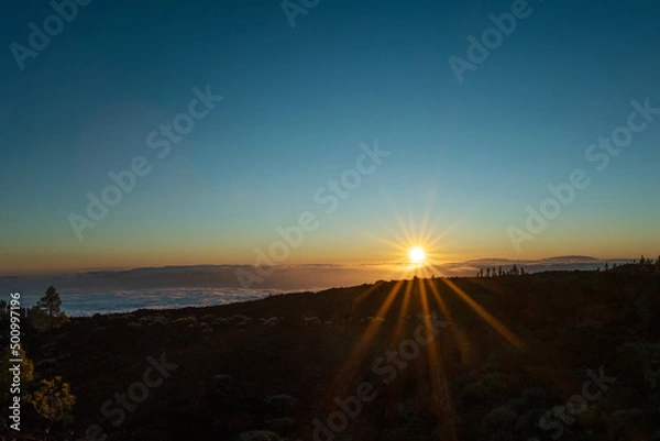 Fototapeta Beautiful sunset over the volcanic landscape and nature up in the mountain. Golden hour and sunlight above the clouds.  Photo taken at Teide national park in Tenerife, Spain.