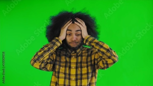 Fototapeta A young man with an African hairstyle on a green background is surprised. Emotions on a colored background.