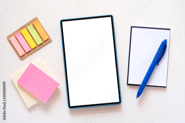 Fototapeta Tablet with copy space, mockup on light beige background. Stationery, stickers, notebook, blue pen around. Minimalism, flat lay, top view.