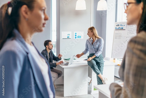Fototapeta Business professionals standing together and having casual discussing in office.