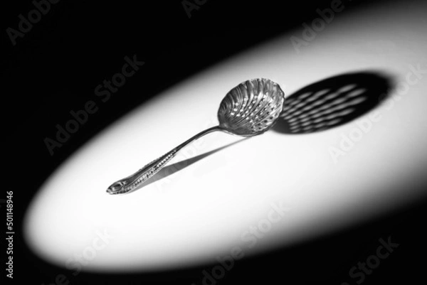Obraz Close up of an Edwardian sifter spoon, in the spotlight, with a dramatic shadow.