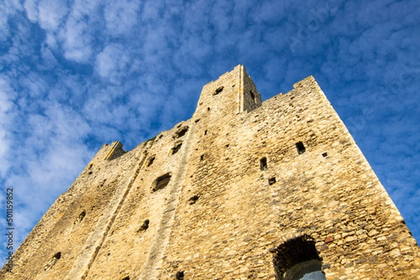 Obraz The tower of Rochester Castle, looking up towards the blue sky, with very light clouds.  The sun is shining on the walls.  October 2021.