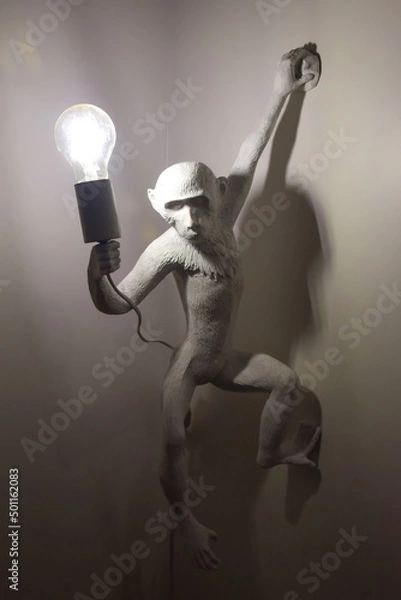 Fototapeta Decorative plaster figurine of a monkey holding a luminous lamp in its paw
